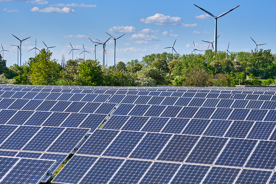 Freiflächen-Solaranlage mit Windrädern Freiflächen-Solaranlage mit Windenergieanlagen und Bäumen im Hintergrund