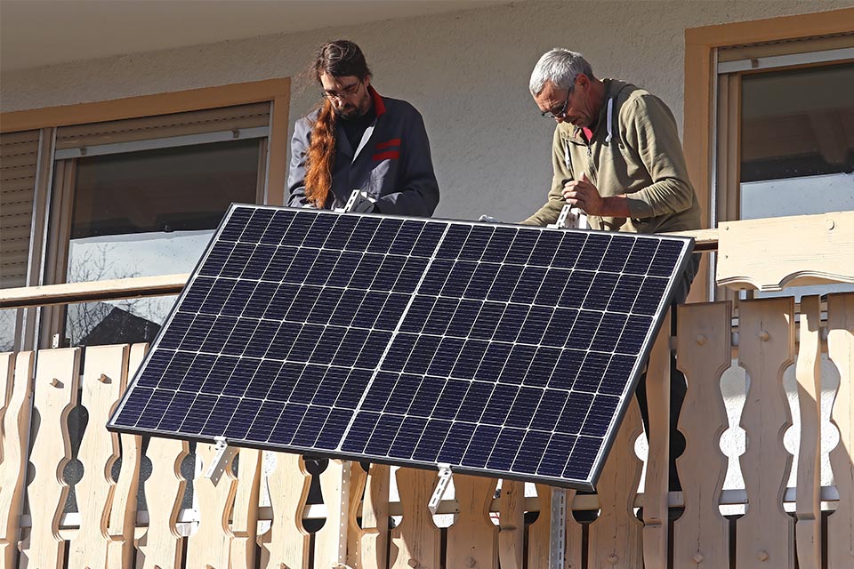 Maenner montieren Balkonkraftwerk Zwei Maenner montieren Solaranlage an Balkon