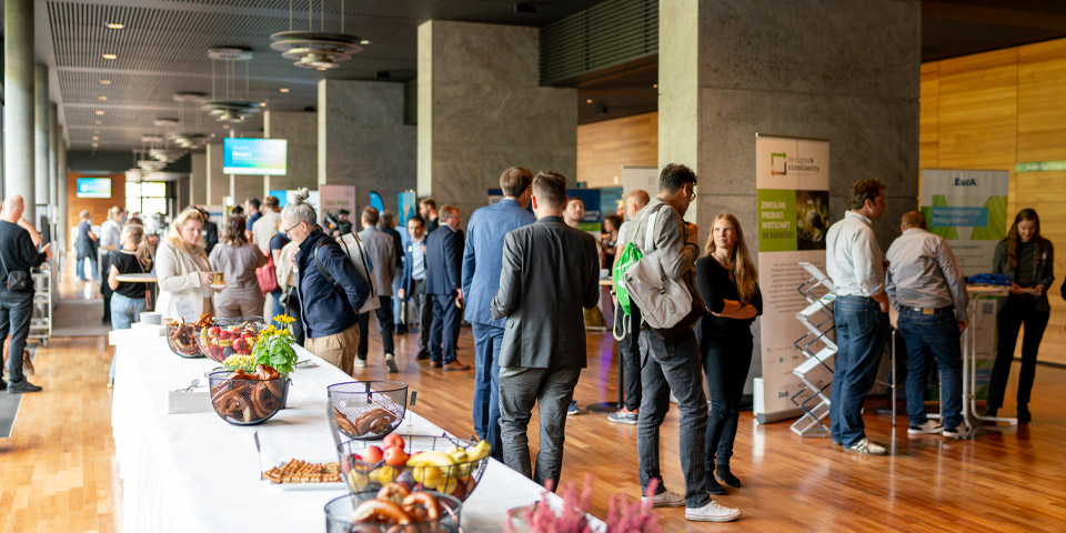 Pause bei der REKON in der Weimarhalle 2025 Pausesituation bei der REKON 2025 in der Weimarhalle, es ist eine Tafel mit weißer Tischdecke zu sehen auf der kleine Snacks aufgestellt wurden. Menschengruppen stehen vereinzelt in der Nähe.