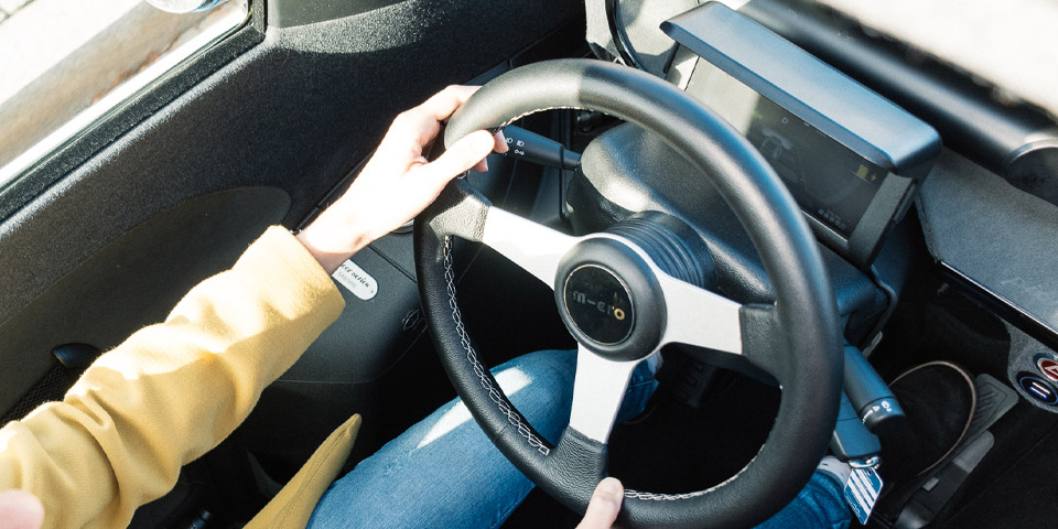 Workshop E-Mobilität Ein E-Auto von oben fotografiert, man sieht das Lenkrad und zwei Arme einer Frau während der Fahrt.