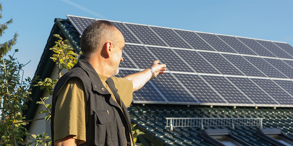 Hauseigentümer mit Solaranlage Hauseigentümer steht vor seinem Einfamilienhaus und zeigt auf die Dachsolaranlage.